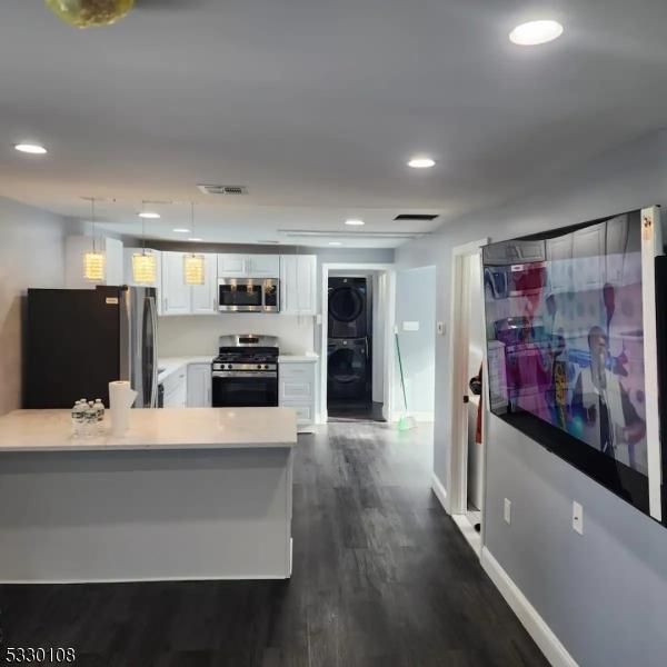 kitchen with hanging light fixtures, kitchen peninsula, stacked washer / drying machine, white cabinets, and appliances with stainless steel finishes