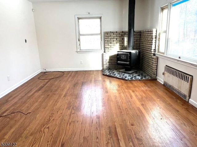 unfurnished living room with hardwood / wood-style floors, a wealth of natural light, a wood stove, and radiator