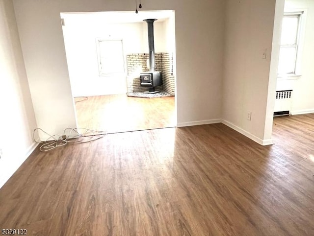 empty room with radiator, dark wood-type flooring, and a wood stove