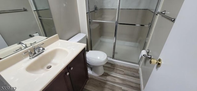 bathroom with hardwood / wood-style flooring, vanity, toilet, and a shower with shower door