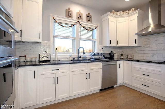 kitchen with white cabinetry, sink, wall chimney range hood, tasteful backsplash, and stainless steel dishwasher