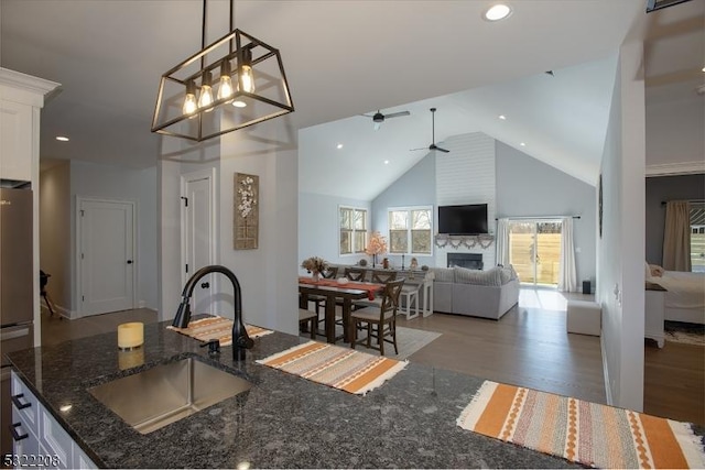 kitchen featuring white cabinets, sink, hanging light fixtures, dark stone countertops, and a large fireplace