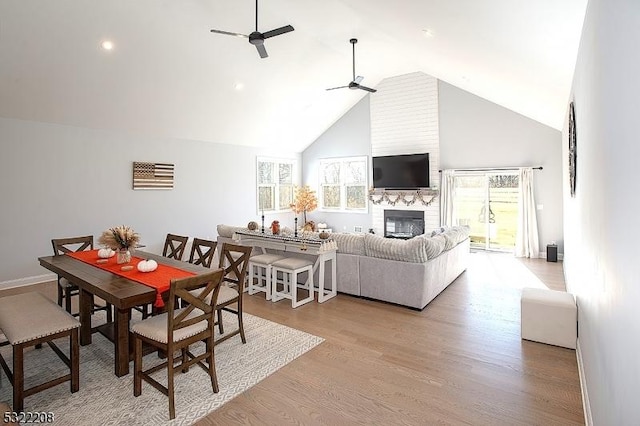 dining space featuring a large fireplace, ceiling fan, a healthy amount of sunlight, and light hardwood / wood-style floors