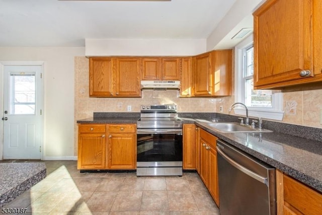 kitchen featuring backsplash, dark stone counters, sink, light tile patterned floors, and appliances with stainless steel finishes