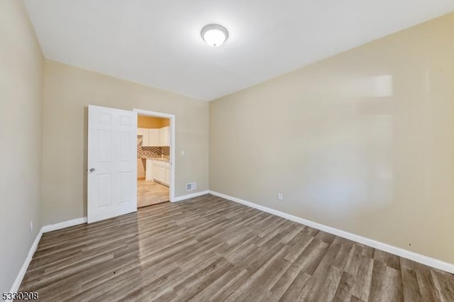 unfurnished bedroom featuring ensuite bathroom and hardwood / wood-style flooring