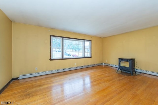 empty room featuring a wood stove, a baseboard radiator, and light hardwood / wood-style flooring