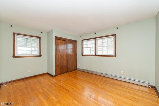 unfurnished bedroom featuring a closet, light hardwood / wood-style floors, multiple windows, and a baseboard heating unit