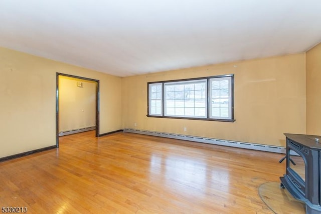 unfurnished living room with a baseboard radiator, a wood stove, and light hardwood / wood-style flooring