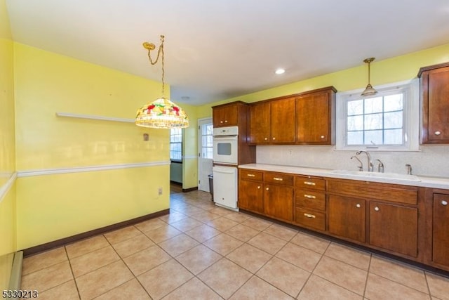 kitchen with decorative backsplash, white oven, sink, pendant lighting, and light tile patterned flooring