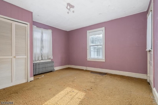 unfurnished bedroom with carpet flooring, a closet, and radiator