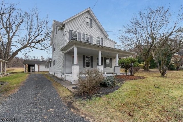 view of front of home featuring a porch, a garage, an outbuilding, and a front lawn