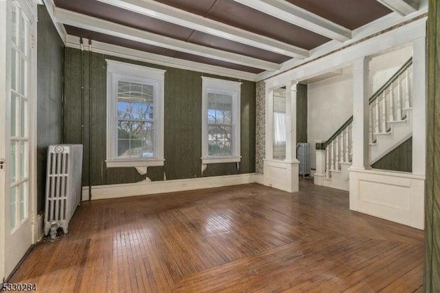 empty room with decorative columns, radiator, beam ceiling, and dark hardwood / wood-style floors