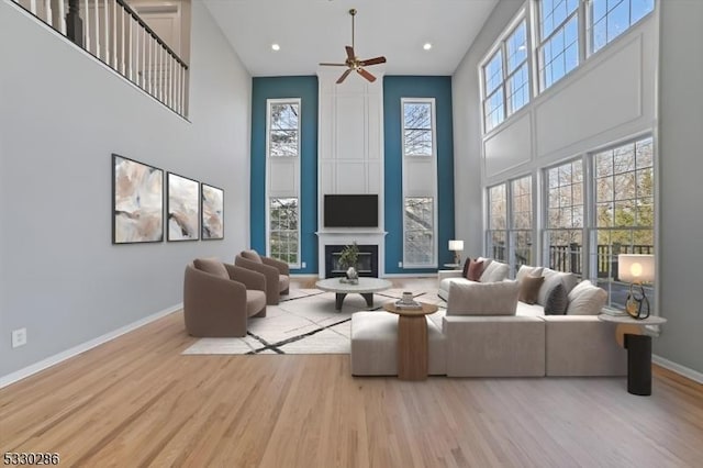 living room featuring a fireplace, a high ceiling, a ceiling fan, wood finished floors, and baseboards