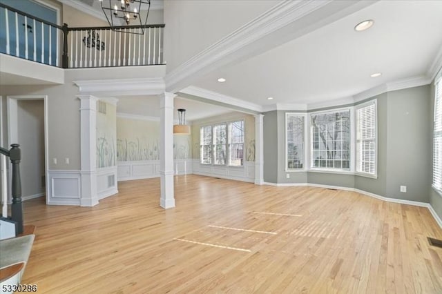 unfurnished living room with crown molding, light wood finished floors, and ornate columns