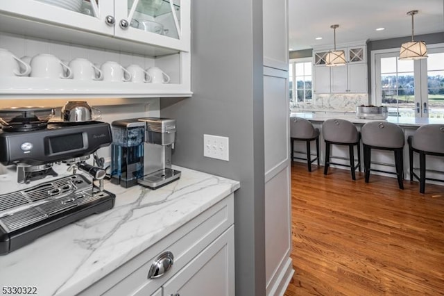 kitchen featuring white cabinets, wood-type flooring, backsplash, and hanging light fixtures