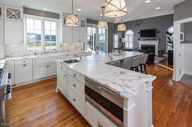 kitchen featuring stainless steel microwave, sink, hanging light fixtures, an island with sink, and tasteful backsplash