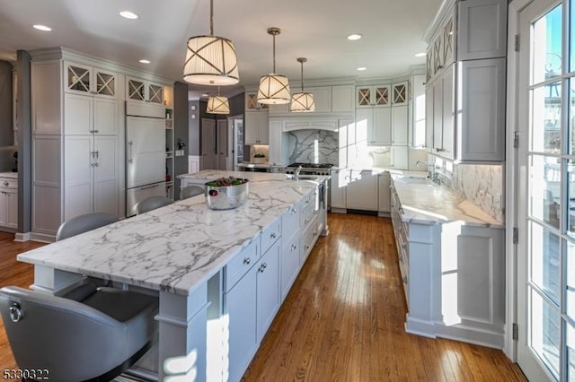 kitchen featuring a large island, hanging light fixtures, premium appliances, a kitchen bar, and hardwood / wood-style flooring