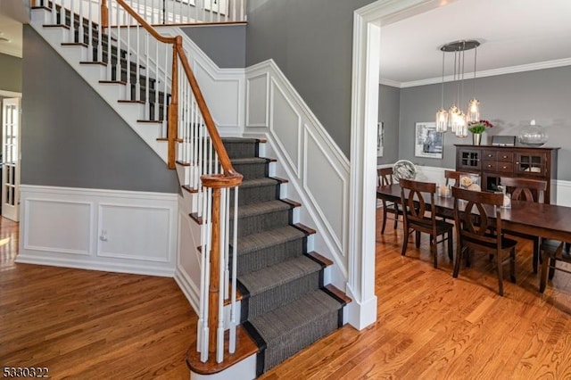 staircase featuring wood-type flooring, an inviting chandelier, and crown molding