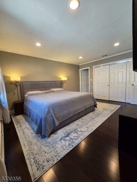 bedroom featuring ornamental molding, recessed lighting, dark wood finished floors, and two closets