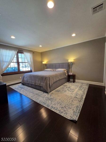 bedroom with ornamental molding, dark hardwood / wood-style floors, and a baseboard heating unit