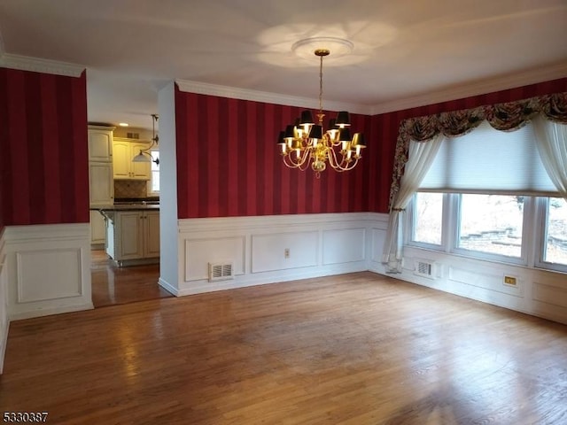 unfurnished dining area with wood-type flooring, an inviting chandelier, and crown molding