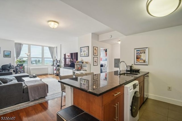 kitchen with sink, stainless steel dishwasher, kitchen peninsula, washer / clothes dryer, and dark stone counters