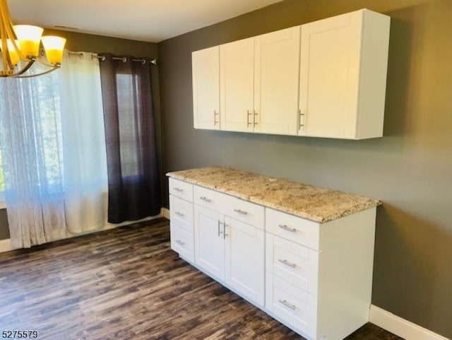 kitchen with white cabinets, a notable chandelier, dark hardwood / wood-style floors, and light stone counters