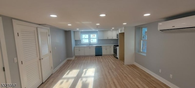 kitchen with sink, light hardwood / wood-style flooring, a wall mounted AC, white cabinets, and appliances with stainless steel finishes