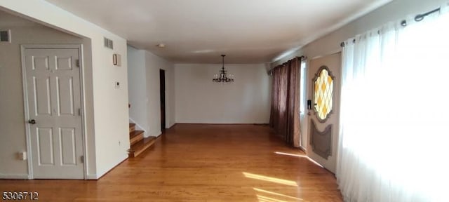 corridor with light hardwood / wood-style floors and an inviting chandelier