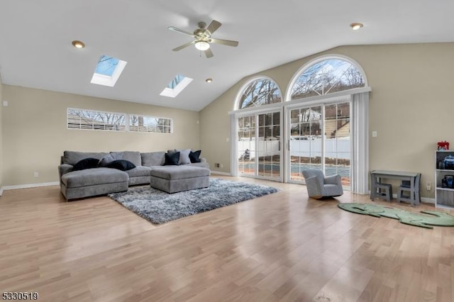 living room with ceiling fan, light wood-type flooring, and vaulted ceiling with skylight