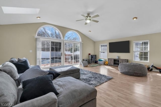 living room with ceiling fan, vaulted ceiling with skylight, a healthy amount of sunlight, and light hardwood / wood-style flooring