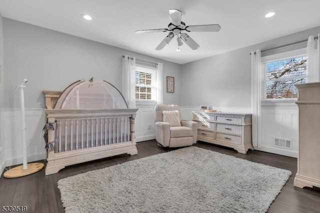 bedroom featuring a nursery area, ceiling fan, and dark hardwood / wood-style floors