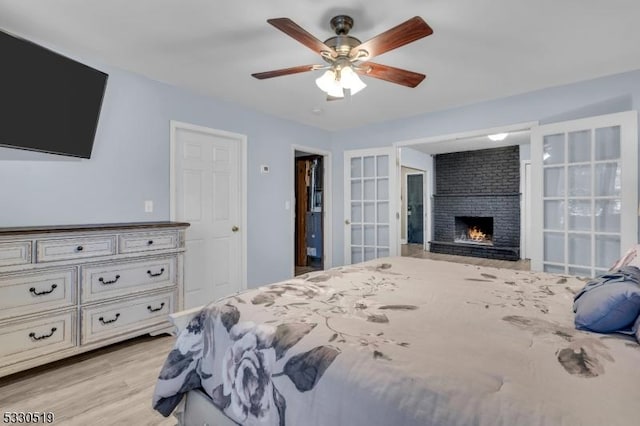 bedroom with french doors, a brick fireplace, ceiling fan, and light hardwood / wood-style flooring