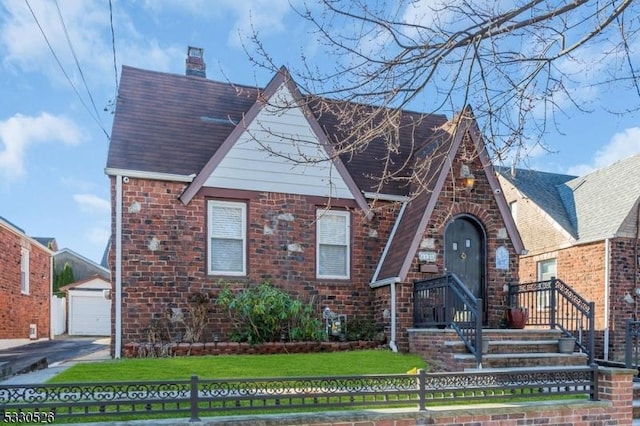 tudor home with a garage, a front lawn, and an outdoor structure