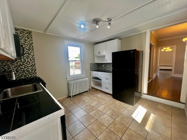 kitchen featuring decorative backsplash, black refrigerator, white cabinetry, and radiator