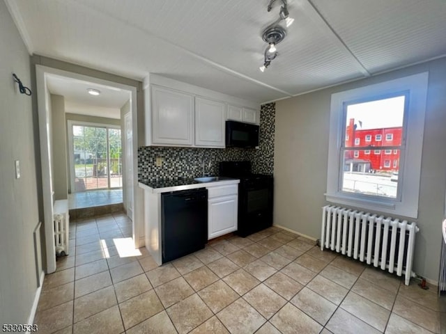 kitchen with backsplash, radiator, black appliances, white cabinets, and light tile patterned flooring