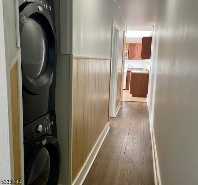 clothes washing area with wood walls, stacked washing maching and dryer, and wood-type flooring