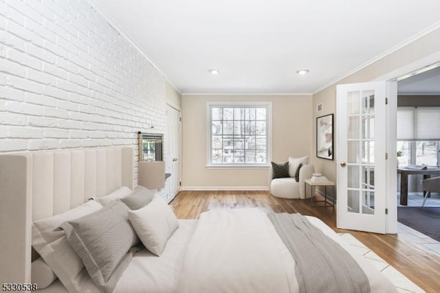 bedroom featuring french doors, light wood-type flooring, crown molding, and brick wall