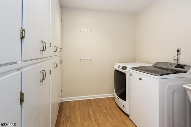 laundry room featuring cabinets, light wood-type flooring, and washing machine and clothes dryer