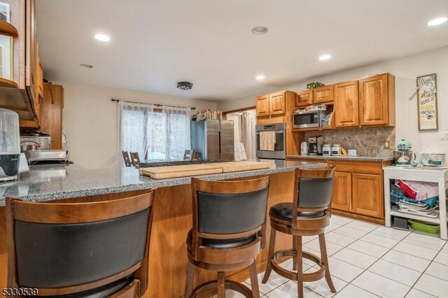 kitchen with backsplash, a kitchen breakfast bar, light tile patterned floors, appliances with stainless steel finishes, and kitchen peninsula