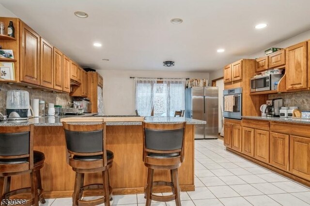 kitchen with backsplash, light tile patterned floors, appliances with stainless steel finishes, a kitchen bar, and kitchen peninsula