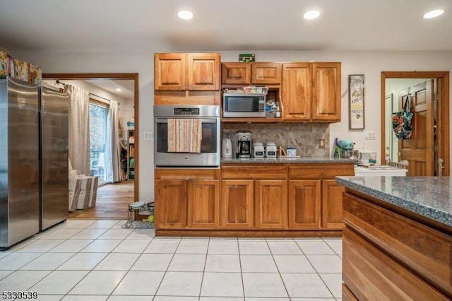 kitchen featuring light tile patterned floors, stainless steel appliances, dark stone counters, and tasteful backsplash