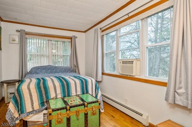 bedroom with a baseboard radiator, cooling unit, ornamental molding, and hardwood / wood-style flooring