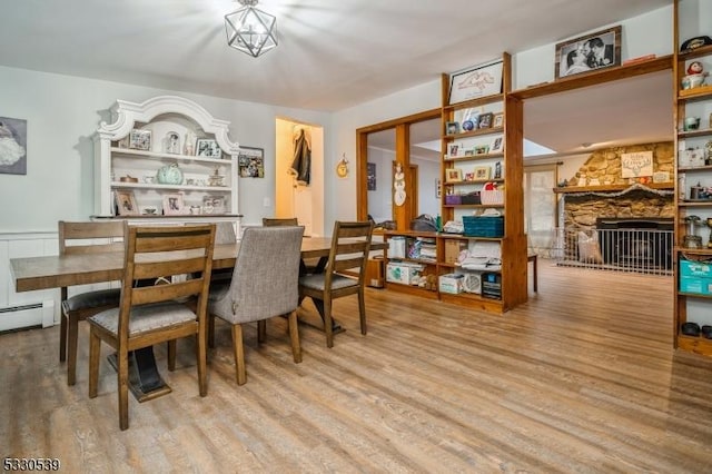 dining room featuring a stone fireplace, a baseboard radiator, and light wood-type flooring