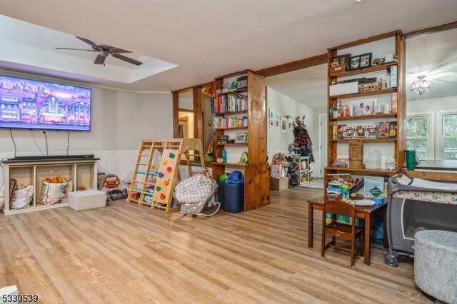 game room with a tray ceiling, light hardwood / wood-style flooring, and ceiling fan