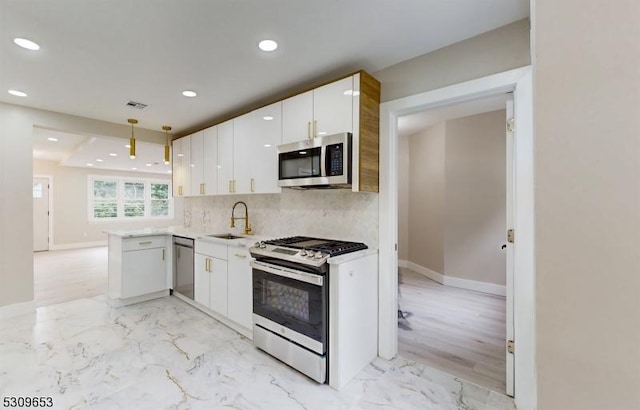 kitchen featuring kitchen peninsula, appliances with stainless steel finishes, sink, white cabinets, and hanging light fixtures