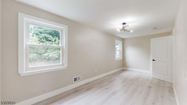 empty room with light hardwood / wood-style floors and a chandelier