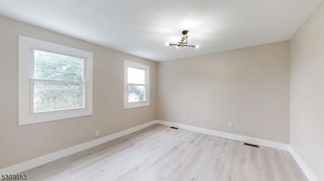 spare room featuring a chandelier and light hardwood / wood-style flooring