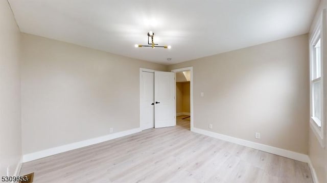 unfurnished room with a wealth of natural light, light hardwood / wood-style floors, and a notable chandelier