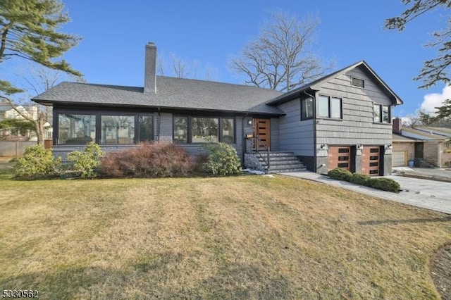 tri-level home featuring a front lawn, roof with shingles, concrete driveway, a garage, and a chimney